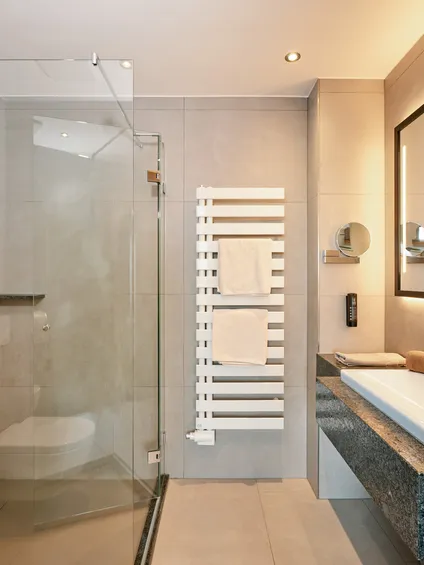 Modernes Hotelbad mit begehbarer Dusche, großem Spiegel und Waschbecken mit Granitplatte