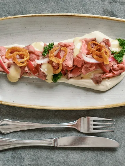 Sandwich aperto con roast beef, cipolle croccanti, prezzemolo e salsa cremosa su piatto in ceramica