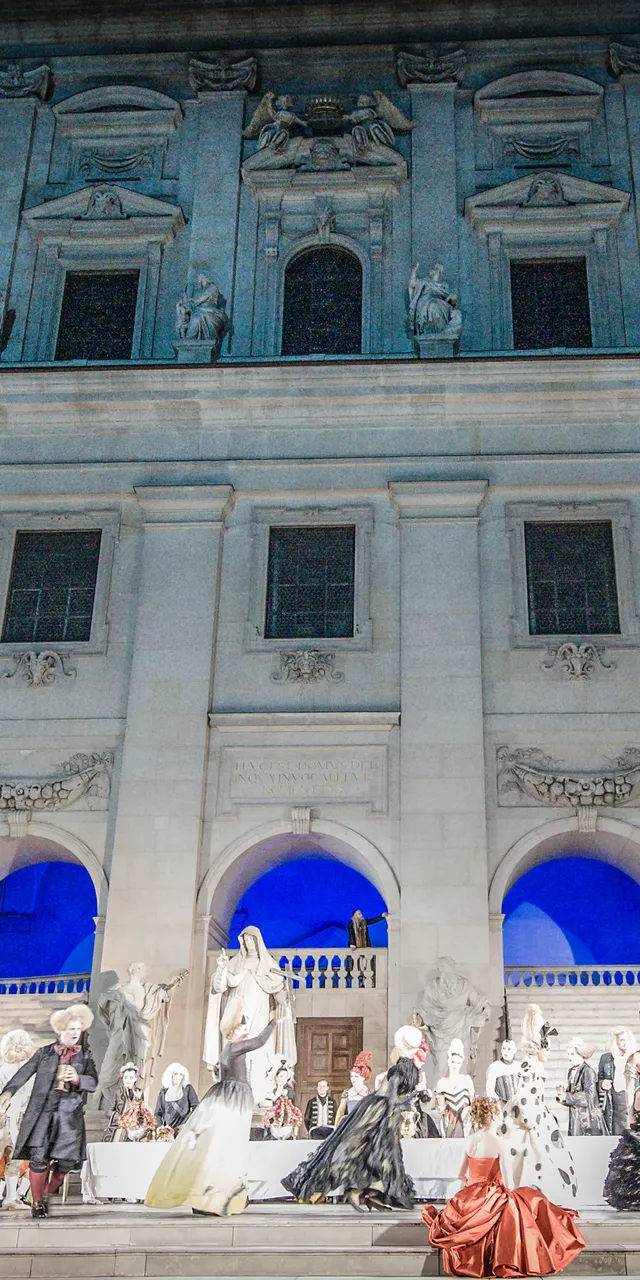 Spettacolo d'opera all'aperto con costumi barocchi davanti a edificio storico in pietra di notte