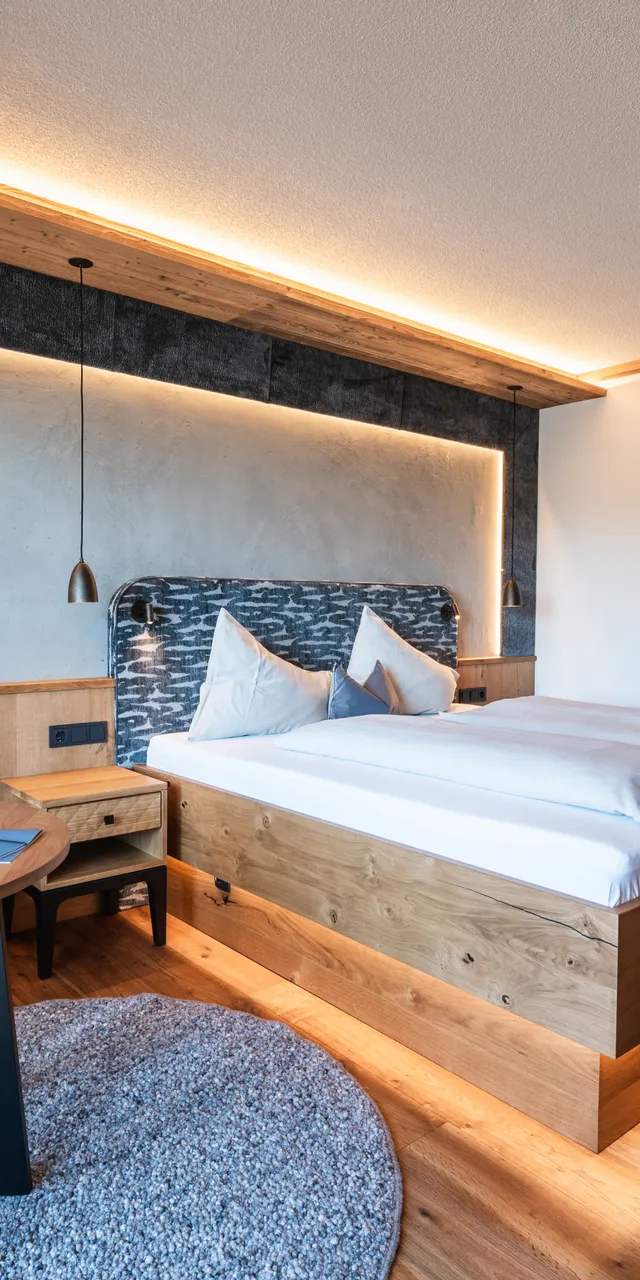 Modernes Hotelzimmer mit Holzboden, großem Bett, blauer Couch und warmer Ambientebeleuchtung