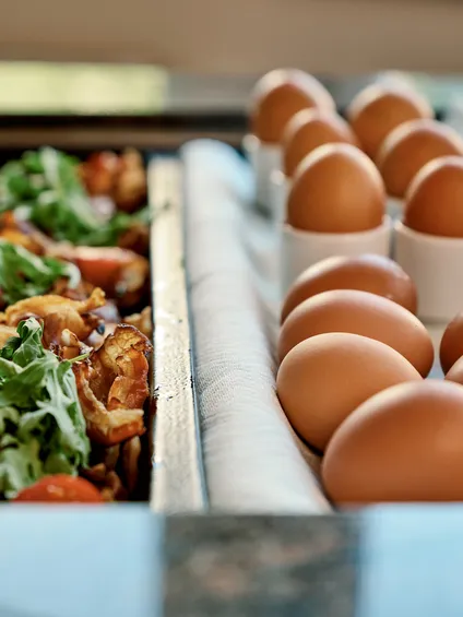 Uova marroni fresche accanto a un vassoio di verdure cotte con erbe sopra