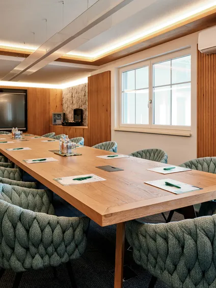 Moderner Konferenzraum mit Holztisch, stilvollen Stühlen und großem Präsentationsbildschirm