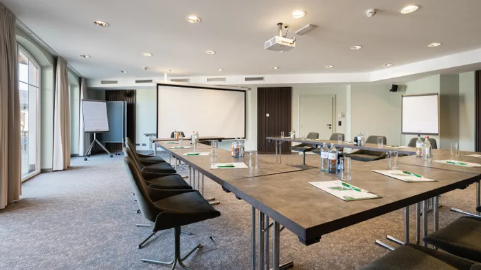 Moderner Konferenzraum mit U-förmigem Tischaufbau, Beamer, Flipcharts und natürlichem Licht