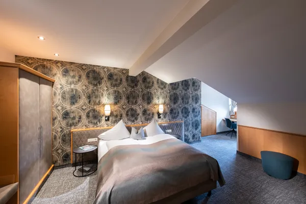 Modern hotel room with double bed, patterned wallpaper, desk, and cozy lighting
