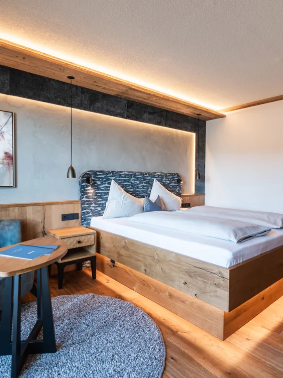 Modernes Hotelzimmer mit Holzboden, großem Bett, blauer Couch und warmer Ambientebeleuchtung